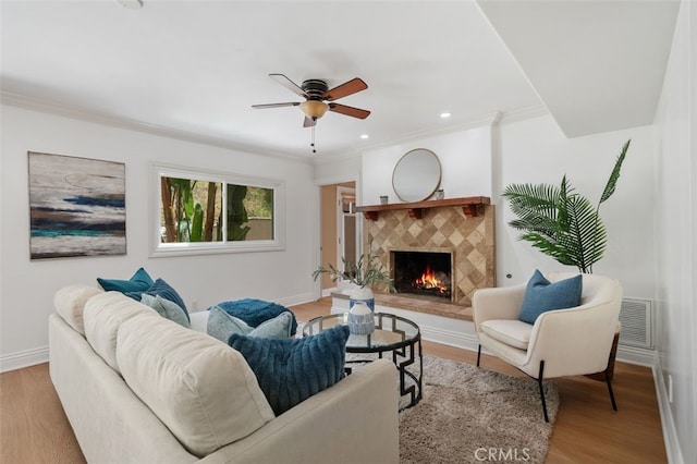 living room featuring a fireplace, wood finished floors, crown molding, ceiling fan, and baseboards