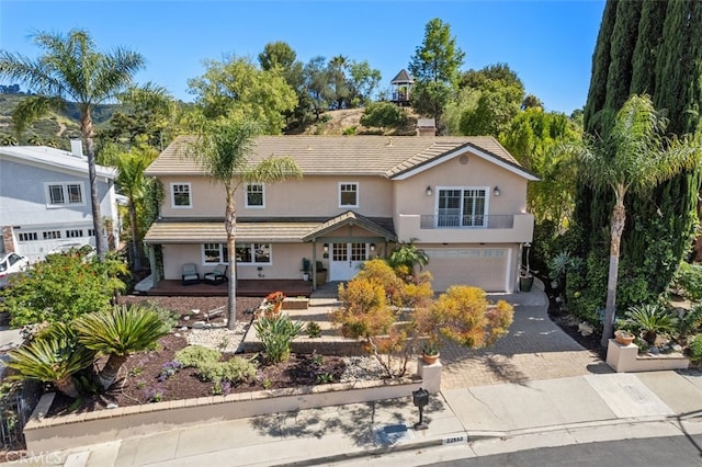 traditional-style house with stucco siding, a garage, decorative driveway, a balcony, and a chimney