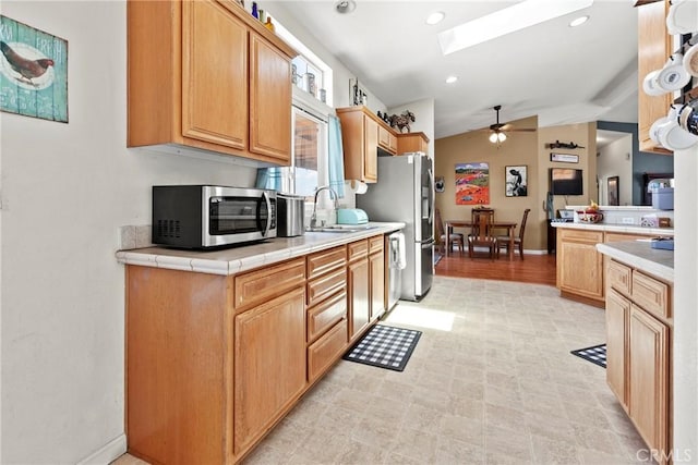 kitchen featuring appliances with stainless steel finishes, a ceiling fan, a sink, a skylight, and vaulted ceiling