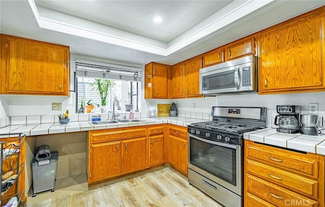 365 W Alameda Ave Unit 203, Burbank, CA 91506 - kitchen with stainless steel appliances, a sink, brown cabinets, light wood-style flooring, and a tray ceiling