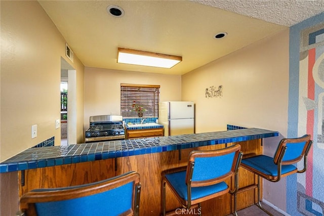 365 W Alameda Ave Unit 203, Burbank, CA 91506 - kitchen with freestanding refrigerator, stainless steel gas range oven, tile countertops, and a kitchen bar