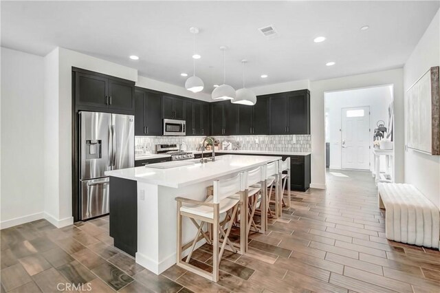 11837 Terra Vista Way, Sylmar, CA 91342 - kitchen with stainless steel appliances, dark cabinets, tasteful backsplash, light countertops, and a kitchen island with sink