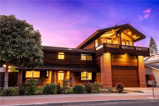 view of front of house featuring a balcony, fence, driveway, and brick siding
