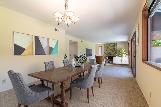 dining area with light carpet, a chandelier, and a stone fireplace