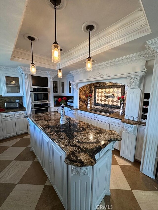 22564 Inspiration Pt, Canyon Lake, CA 92587 - kitchen with a tray ceiling, decorative columns, glass insert cabinets, a kitchen island, and crown molding