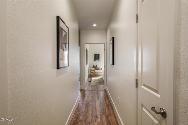 corridor featuring dark wood finished floors, baseboards, recessed lighting, and a textured wall