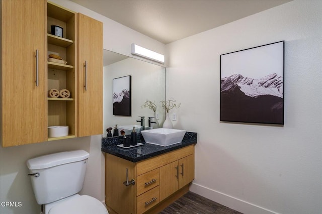 half bath featuring wood finished floors, baseboards, toilet, and vanity