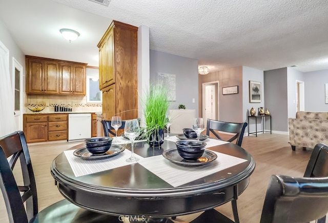 dining area with light wood-type flooring, a textured ceiling, and baseboards