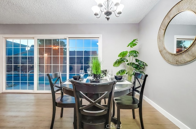 dining area featuring a textured ceiling, wood finished floors, baseboards, and a chandelier