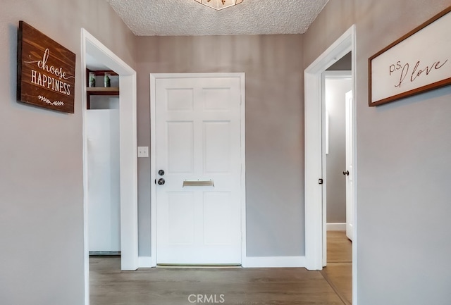 hall featuring wood finished floors, a textured ceiling, and baseboards