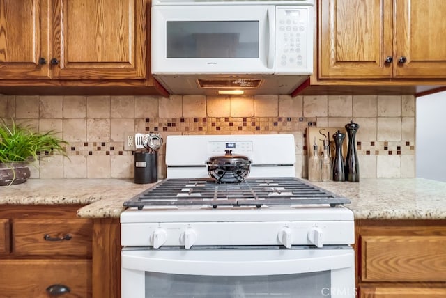 kitchen with white appliances, brown cabinets, tasteful backsplash, and light stone counters