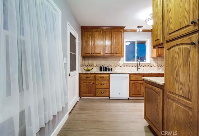 kitchen with white dishwasher, a sink, light wood finished floors, backsplash, and brown cabinets