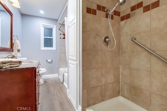 full bathroom featuring a tile shower, vanity, wood finished floors, toilet, and recessed lighting