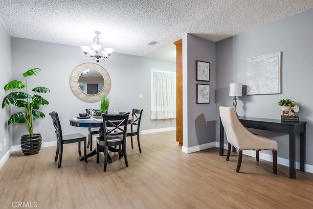 dining space featuring a chandelier, light wood finished floors, baseboards, and a textured ceiling