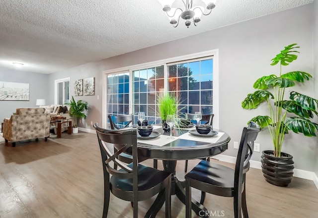 dining space featuring wood finished floors, a chandelier, a textured ceiling, and baseboards