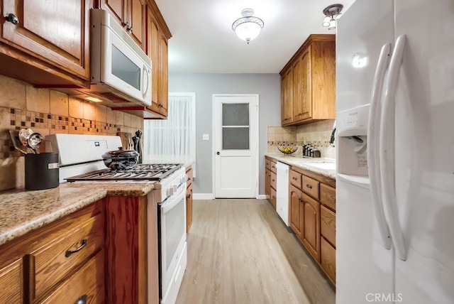 kitchen with white appliances, tasteful backsplash, light wood finished floors, and brown cabinetry
