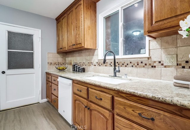 kitchen featuring dishwasher, a sink, light wood-type flooring, brown cabinetry, and decorative backsplash