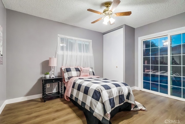 bedroom featuring wood finished floors, a textured ceiling, baseboards, a ceiling fan, and access to exterior