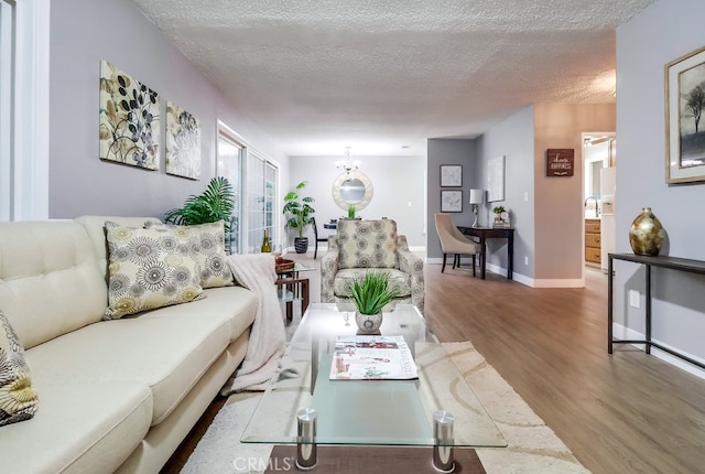 living area featuring wood finished floors, a textured ceiling, a chandelier, and baseboards