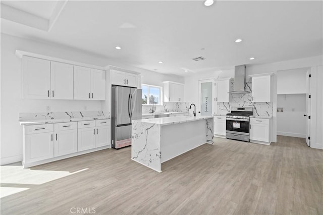 kitchen featuring appliances with stainless steel finishes, wall chimney range hood, a sink, white cabinets, and recessed lighting