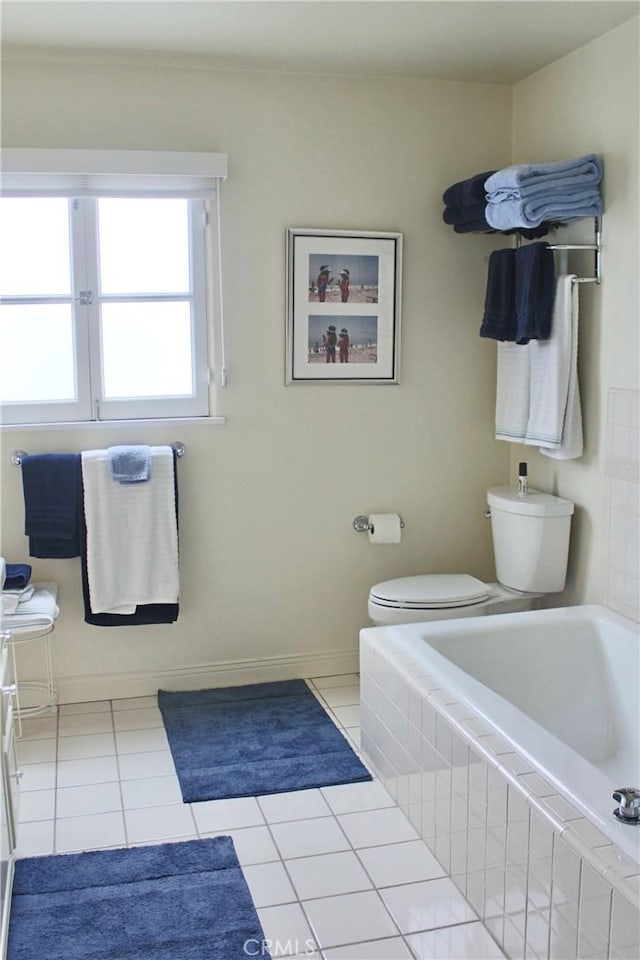 full bathroom with toilet, a relaxing tiled tub, tile patterned floors, and baseboards
