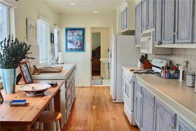 kitchen featuring white appliances, tile countertops, a sink, light wood-style floors, and decorative backsplash