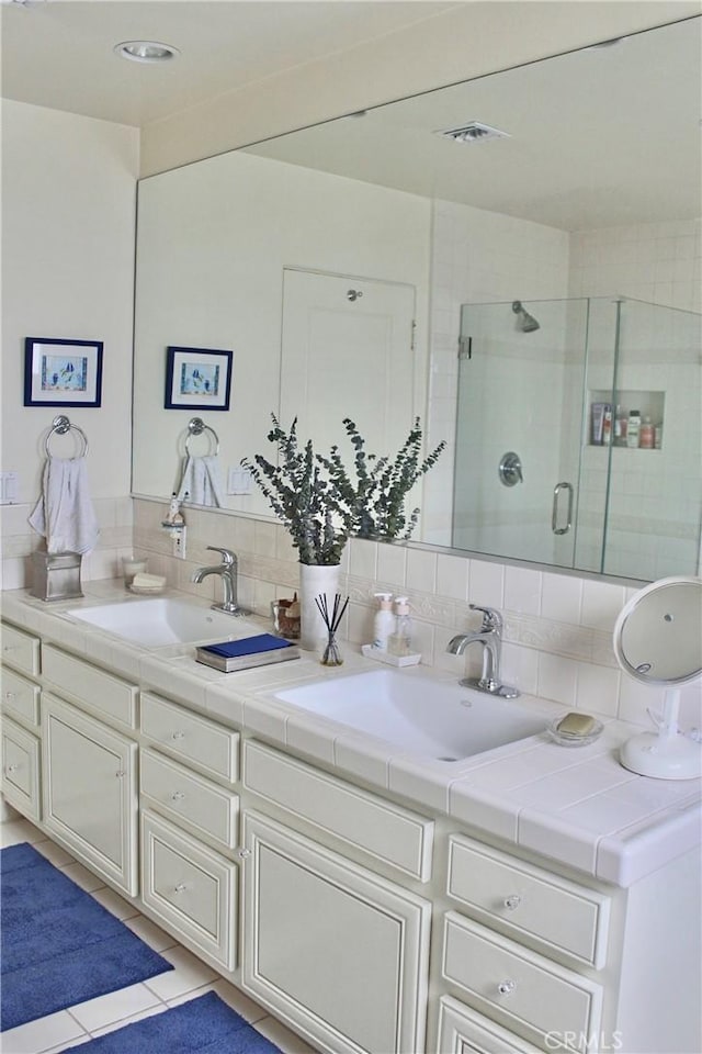bathroom with a shower stall, double vanity, backsplash, and tile patterned flooring