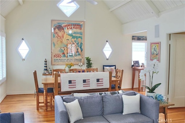living room featuring light wood-style floors, plenty of natural light, beam ceiling, high vaulted ceiling, and baseboards