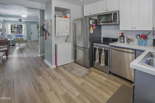 kitchen with stainless steel appliances, stacked washer / drying machine, light wood-type flooring, light countertops, and a ceiling fan