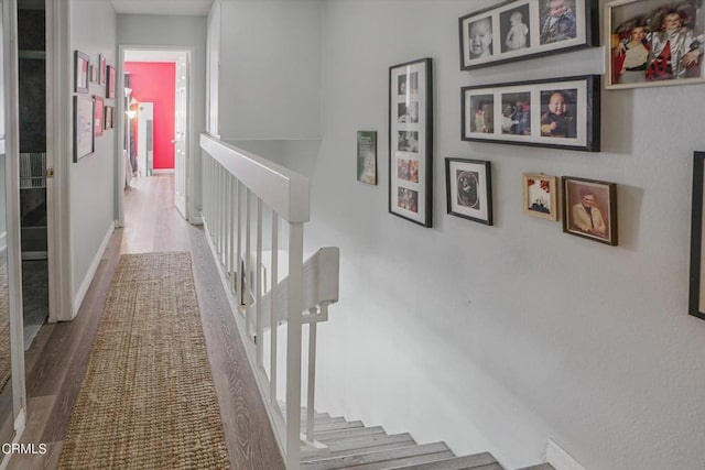 corridor featuring wood finished floors, an upstairs landing, and baseboards