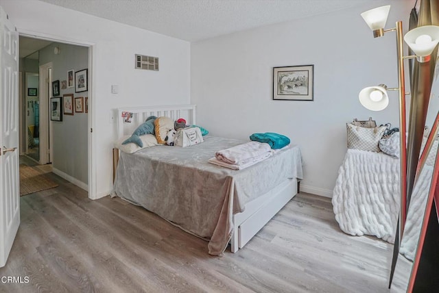 bedroom featuring wood finished floors, a textured ceiling, and baseboards