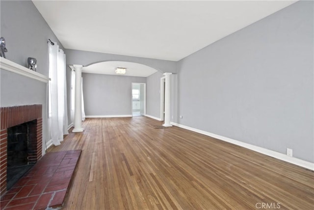 5939 5th Ave, Hyde Park, CA 90043 - unfurnished living room featuring decorative columns, a brick fireplace, wood finished floors, and arched walkways