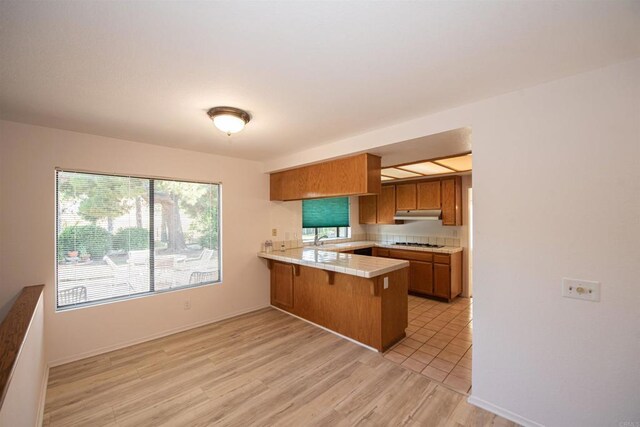2432 Live Oak Rd, Escondido, CA 92029 - kitchen with a peninsula, brown cabinetry, a sink, white gas stovetop, and under cabinet range hood