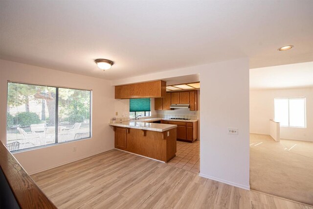 2432 Live Oak Rd, Escondido, CA 92029 - kitchen with brown cabinetry, a peninsula, under cabinet range hood, light countertops, and a kitchen breakfast bar