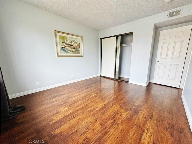 unfurnished bedroom with wood finished floors, a closet, a textured ceiling, and baseboards