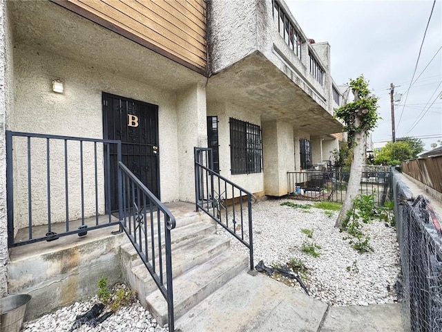 doorway to property with stucco siding and fence