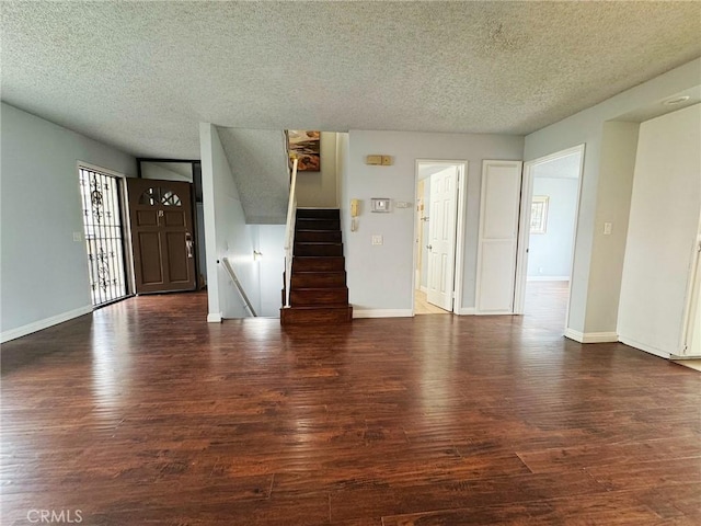 unfurnished living room with a textured ceiling, wood finished floors, stairway, and baseboards