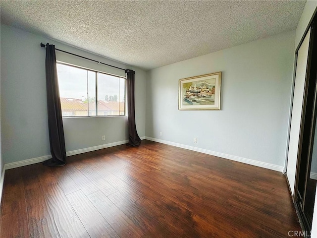 unfurnished room with dark wood-type flooring, a textured ceiling, and baseboards