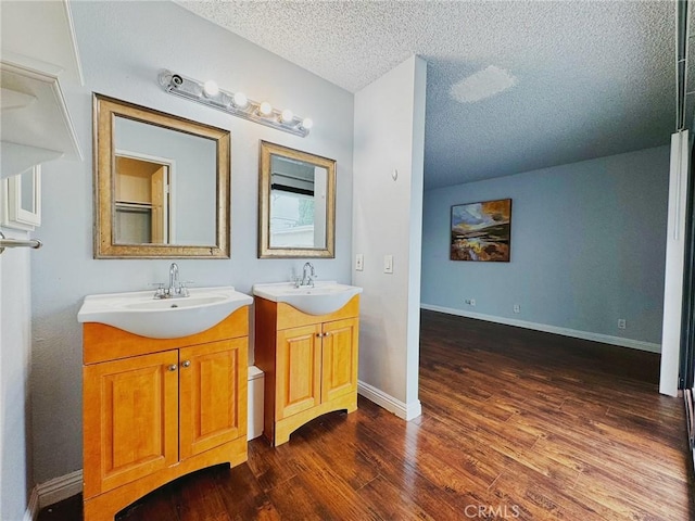 bathroom with wood finished floors, a textured ceiling, two vanities, and baseboards