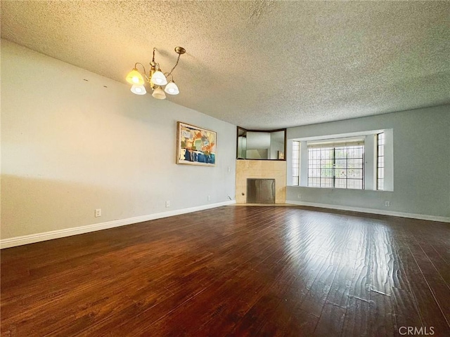 unfurnished living room featuring a textured ceiling, a chandelier, hardwood / wood-style floors, a tile fireplace, and baseboards