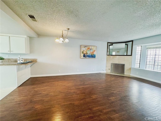 unfurnished living room featuring a textured ceiling, a chandelier, dark wood-type flooring, baseboards, and a tile fireplace