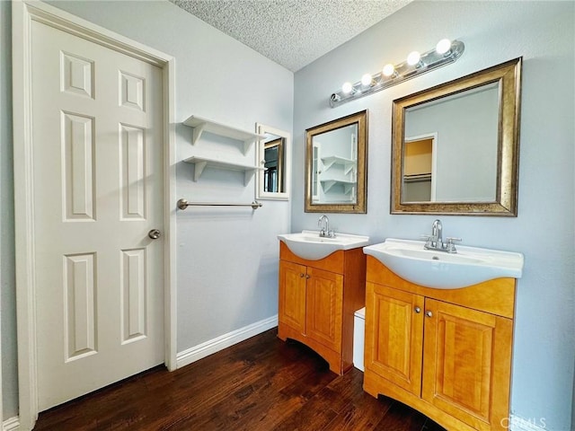 bathroom with wood finished floors, a textured ceiling, two vanities, and baseboards