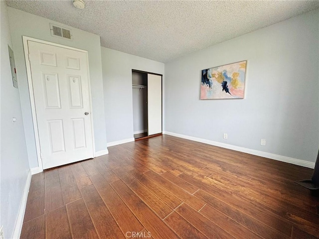 unfurnished bedroom with dark wood-style floors, baseboards, a textured ceiling, and a closet
