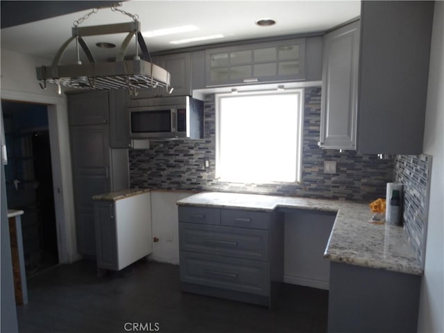 kitchen with stainless steel microwave, tasteful backsplash, gray cabinetry, and light stone countertops