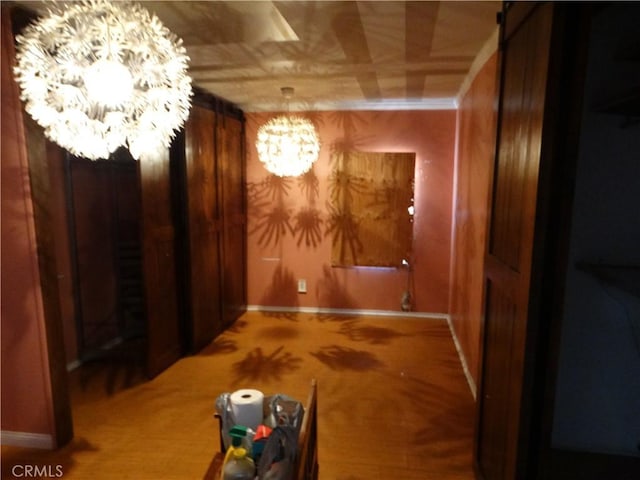 hallway featuring a chandelier, baseboards, and carpet flooring