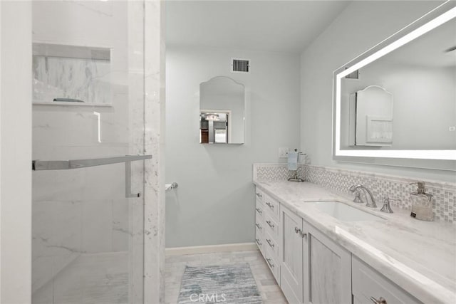 bathroom featuring vanity, a marble finish shower, and tasteful backsplash