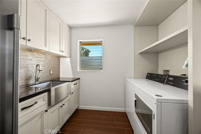 clothes washing area with cabinet space, washing machine and dryer, baseboards, and dark wood finished floors