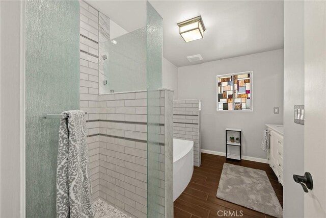 bathroom with wood finished floors, tiled shower, vanity, a freestanding bath, and baseboards