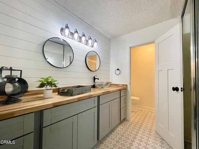 full bathroom with tile patterned floors, toilet, double vanity, a textured ceiling, and wooden walls