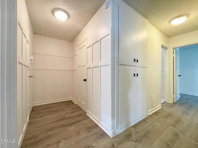hallway featuring a textured ceiling, wood finished floors, and baseboards